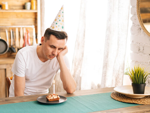 Upset young man sitting at the birthday cake and looking with sad eyes on it.