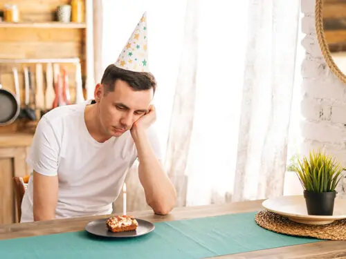 Upset young man sitting at the birthday cake and looking with sad eyes on it.
