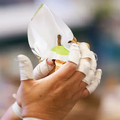 A photo of a gold pear being wrapped in foil by a pair of hands.