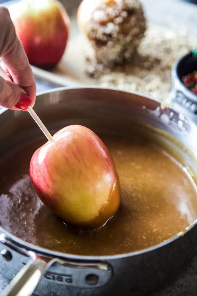 A photo of caramel apples diy apple being dipped into caramel sauce