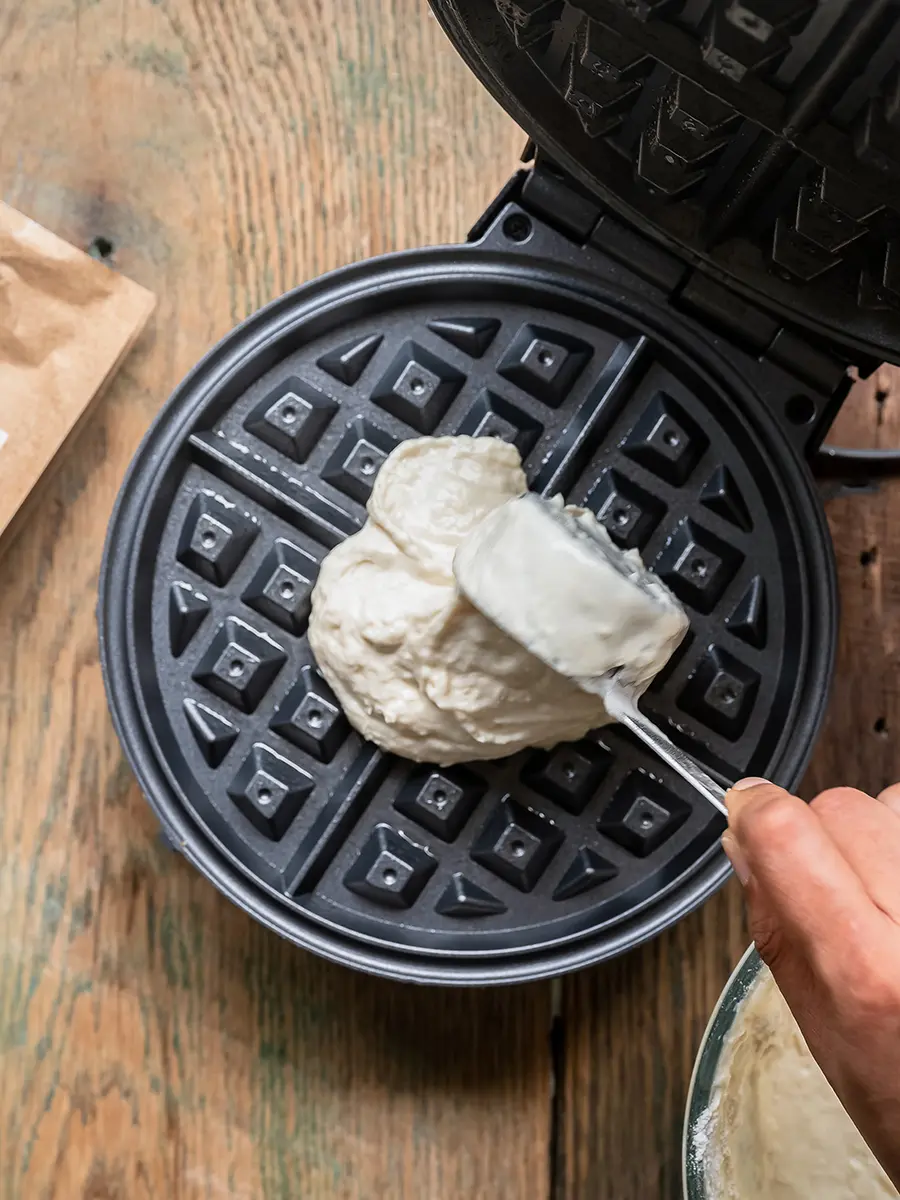 How to make waffles with pancake mix with a hand pouring batter onto a waffle iron.