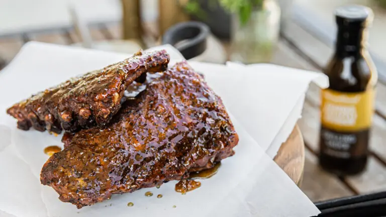 Korean BBQ ribs on a platter with a bottle of grilling sauce next to it.