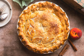 Peach pie with peaches and cutlery surrounding it.