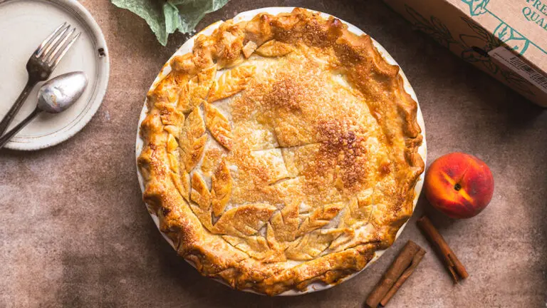 Peach pie with peaches and cutlery surrounding it.