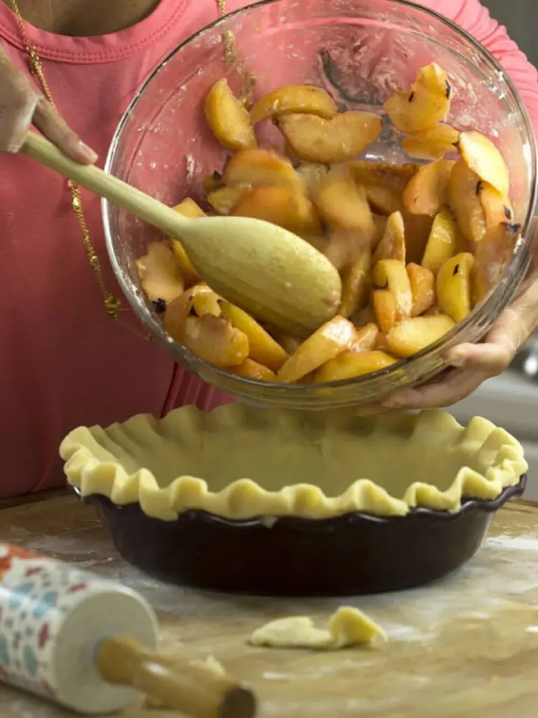 Person pouring plums into a pie dish.