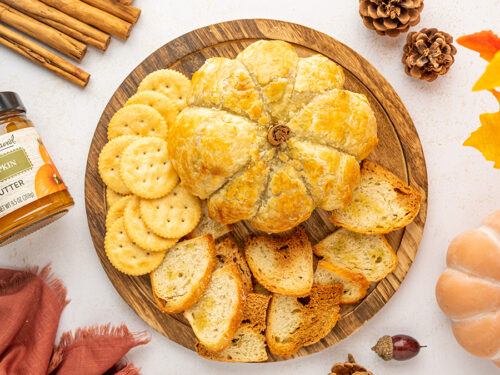 Pumpkin baked brie on a platter with crackers and sliced baguette.