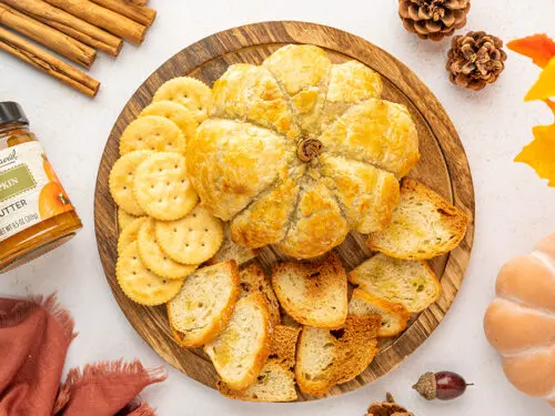 Pumpkin baked brie on a platter with crackers and sliced baguette.