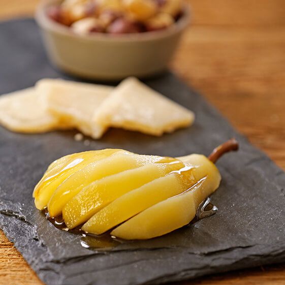 A photo of poached pears with a sliced beer poached pear on top of a slate cutting board with cheese and nuts in the background.