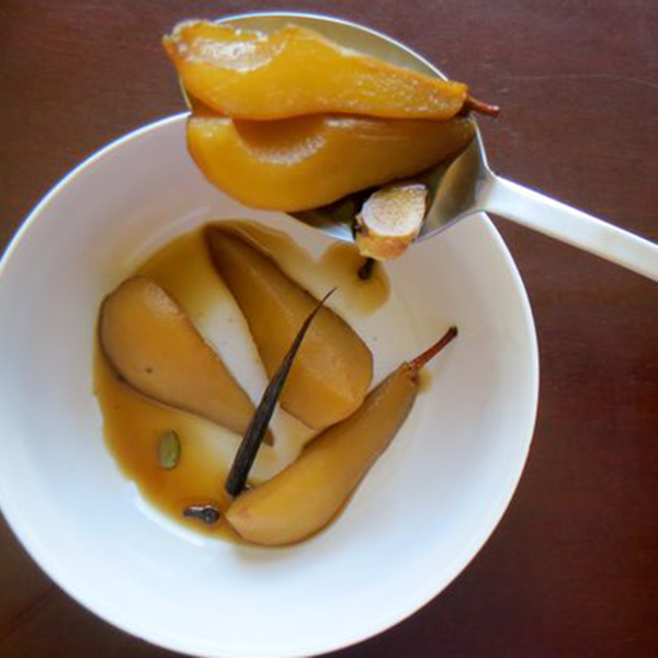 A photo of a sliced bourbon masala poached pear in a bowl with a spoon lifting a few slices towards the camera.