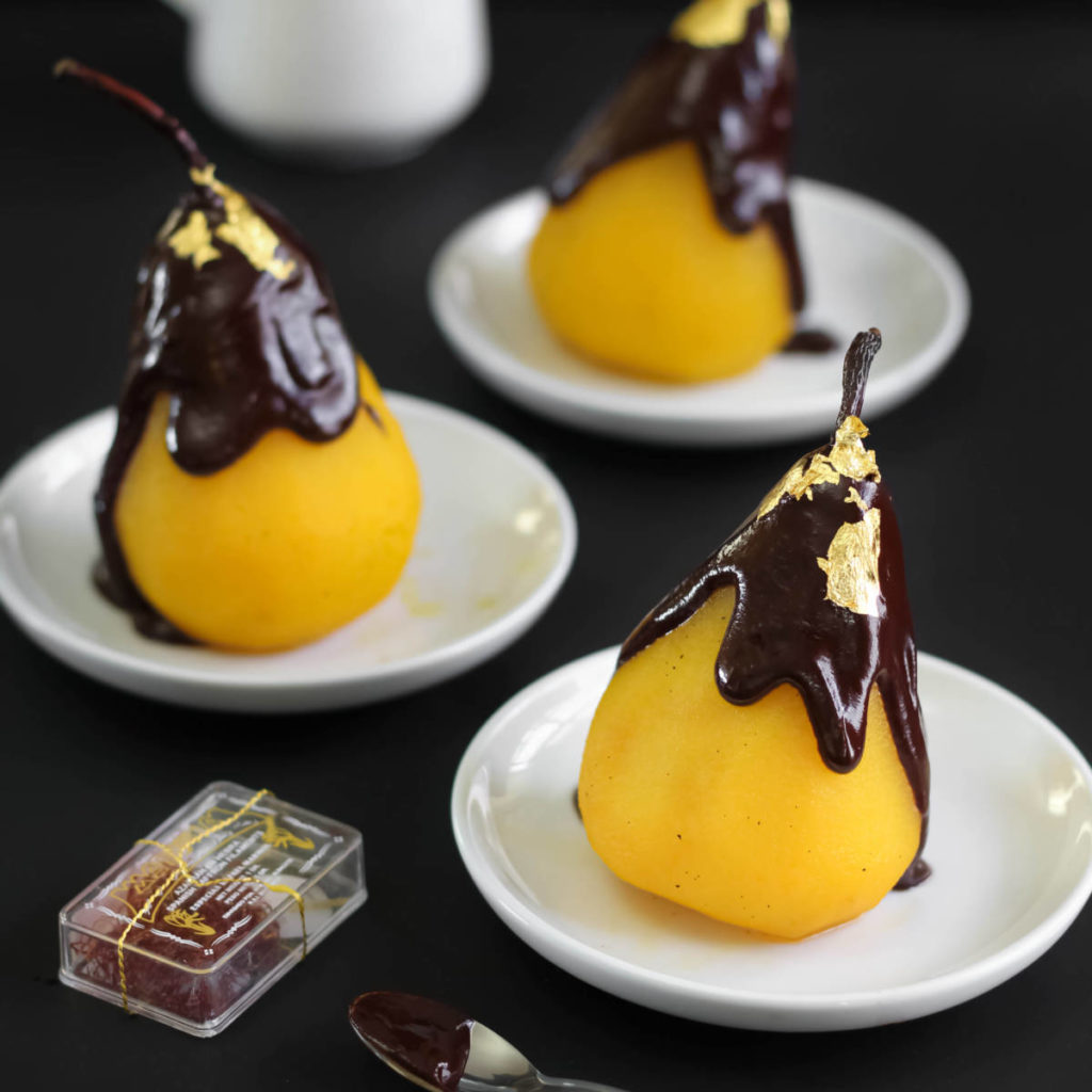 A photo of poached pears with three saffron poached pears covered in chocolate sitting on three plates.