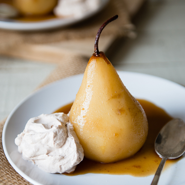 A photo of poached pears with a vanilla chai poached pear sitting on a plate with a dollop of whipped cream.