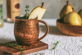Moscow Mule with a slice of pear as garnish with pears and bottles in the background.