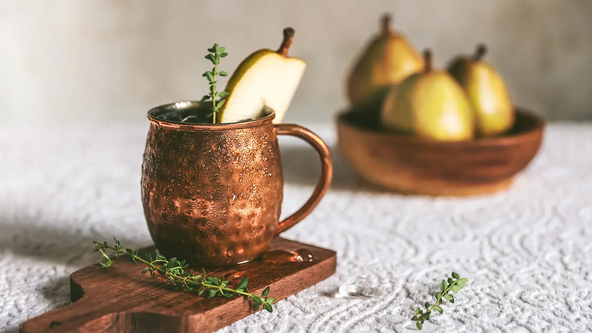 Moscow Mule with a pear garnish with pears in the background.