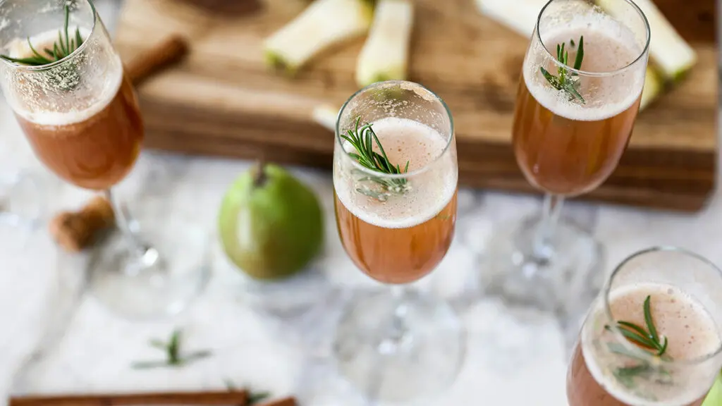 A photo of pear bellini with several glasses on a marble counter with a pear in the background