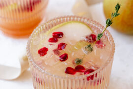 Pear kombucha mocktail in a glass with a slice of pear, pomegranate seeds, and thyme.