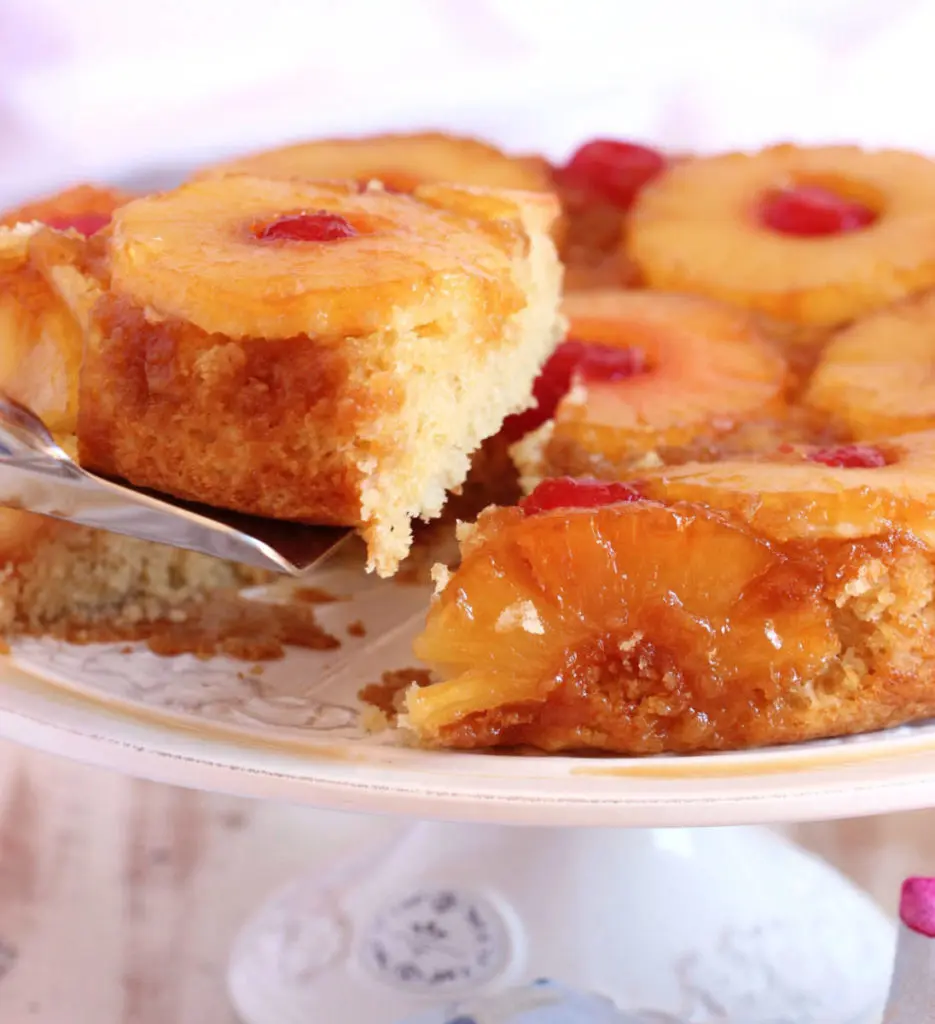 Pineapple Upside Down Cake on a platter with a slice being lifted out.