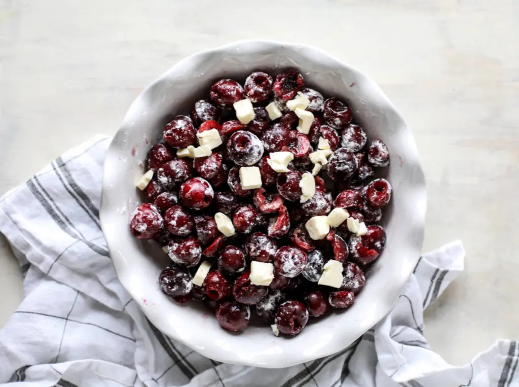 A photo of cherry crisp with a bowl of pitted cherries and cubes of butter.