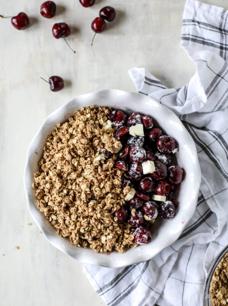 A photo of cherry crisp with a bowl of pitted cherries and cubed butter covered with rolled oats
