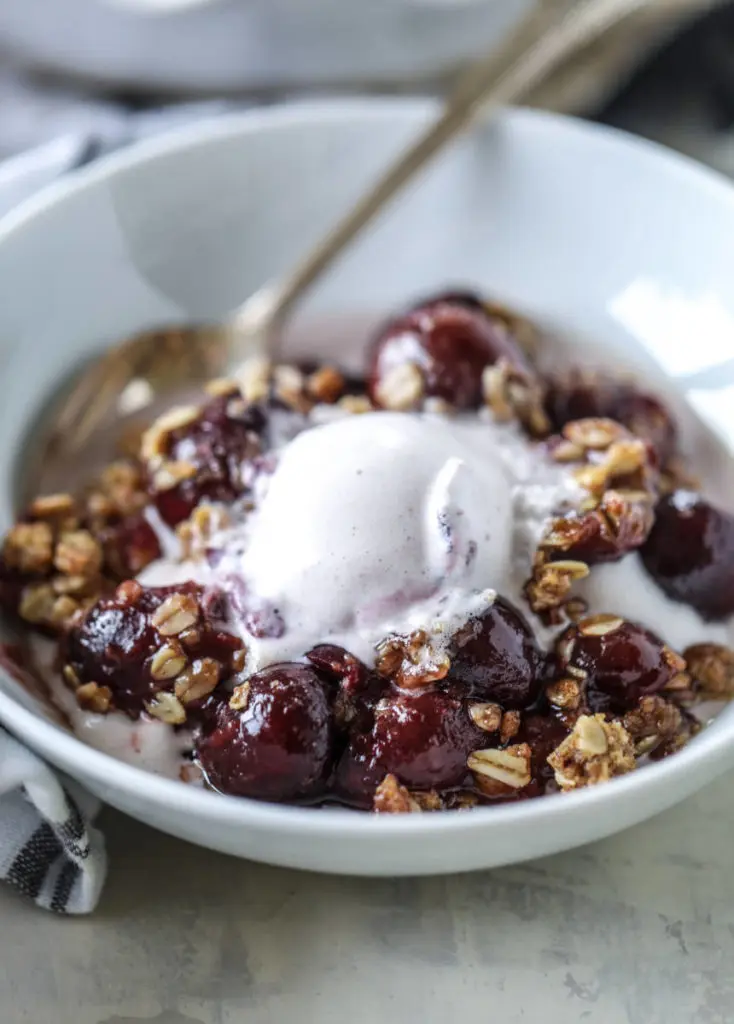 A photo of cherry crisp with a bowl of cherry crisp and ice cream.