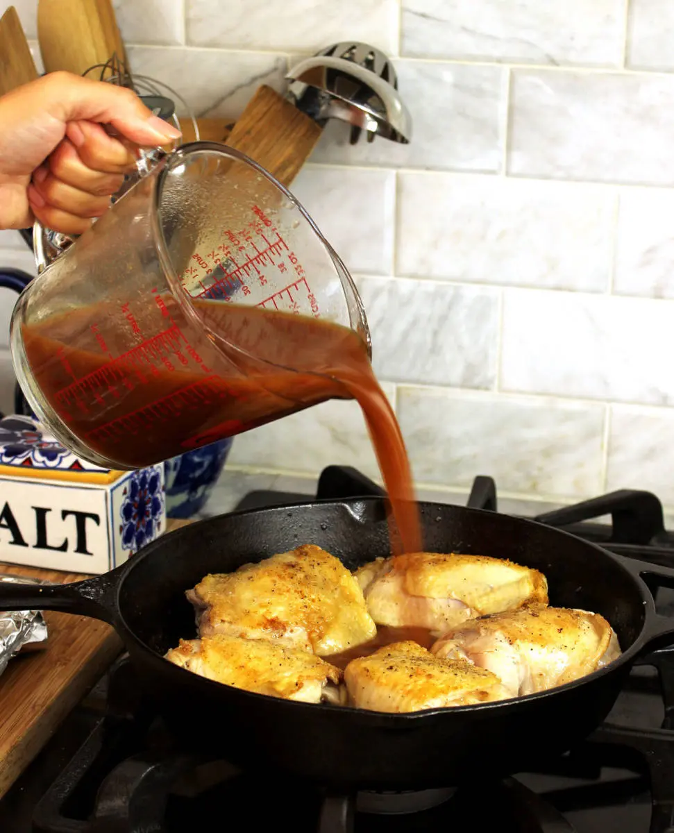 Pepper & Onion Relish Chicken image - hand pouring relish onto chicken in a skillet on a stove.