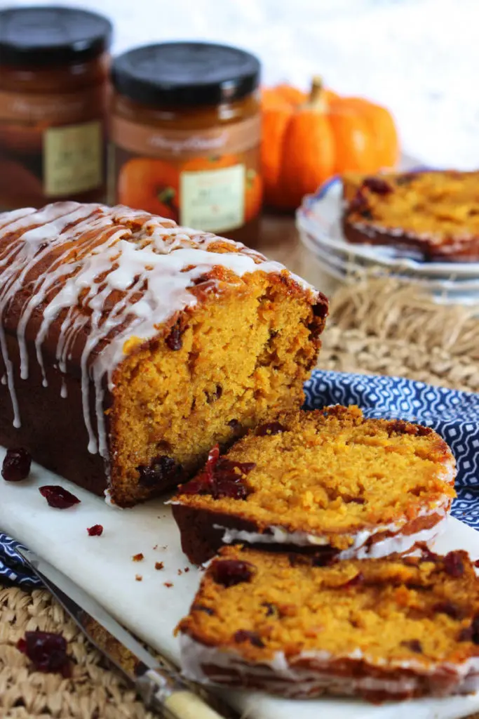 Loaf of pumpkin bread with cranberries sliced on a plate.