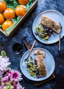 A photo of a salmon recipe with two plates of cooked salmon with slaw next to a box of oranges.