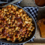 A photo of baked beans recipe with a bowl of baked beans next to a bottle of bbq sauce