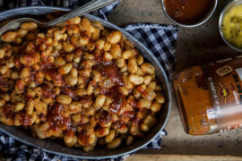 A photo of baked beans recipe with a bowl of baked beans next to a bottle of bbq sauce