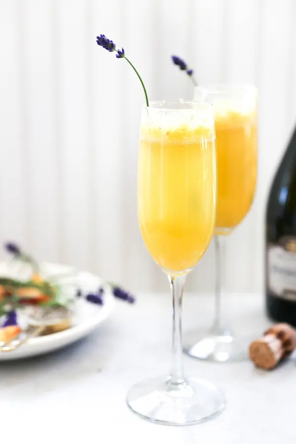 Photo of a peach bellini in a champagne flute with a sprig of lavender coming out.