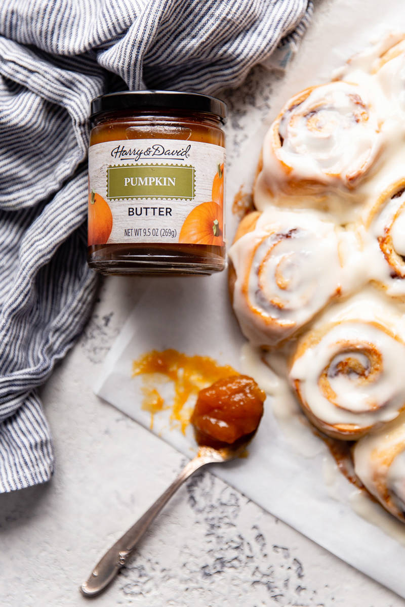 Jar of pumpkin butter next to a tray of iced cinnamon roll.s