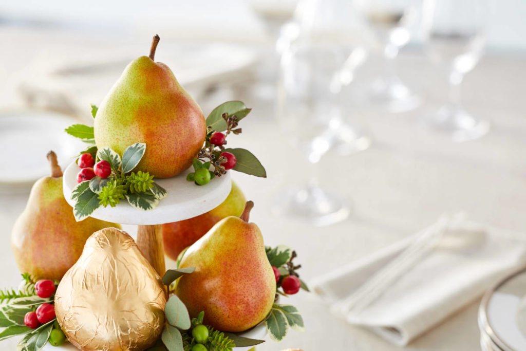 A photo of Christmas pears with a stack of pears on a stand decorated with Christmas greenery.
