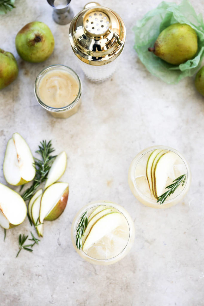 Gin fizz cocktails with pear slices and cocktail shaker next to it.