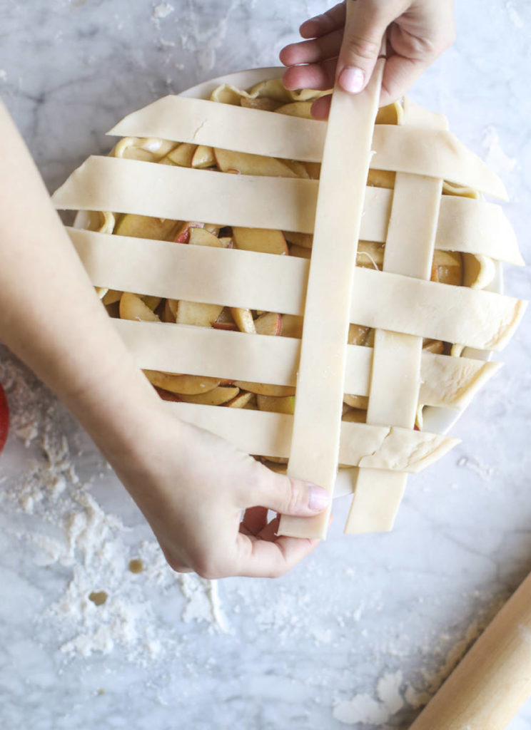 Unbaked apple pie recipe with hands making a lattice crust.