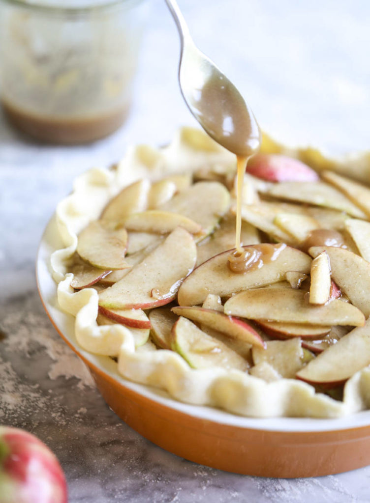 Unbaked apple pie recipe being drizzled with caramel sauce.