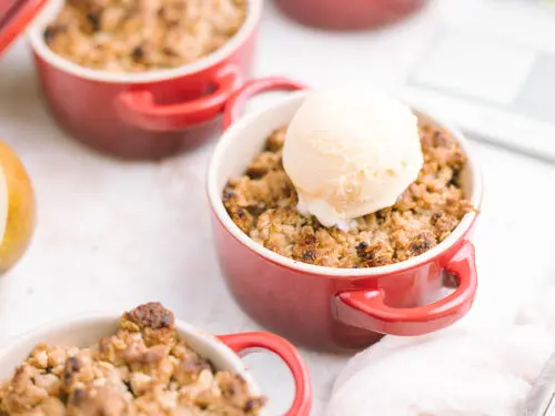 Pear crumble in small ramekin topped with ice cream.