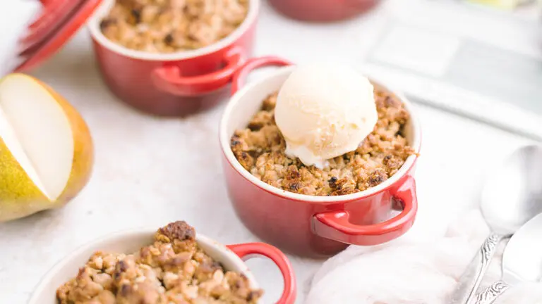 Pear crumble in small ramekin topped with ice cream.