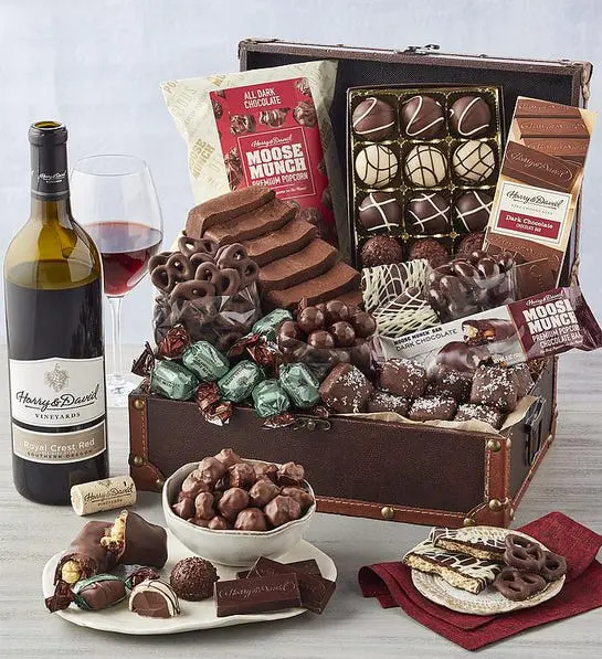 A photo of birthday gift ideas with a box of chocolate truffles, cake, and other snacks next to a bottle of wine.