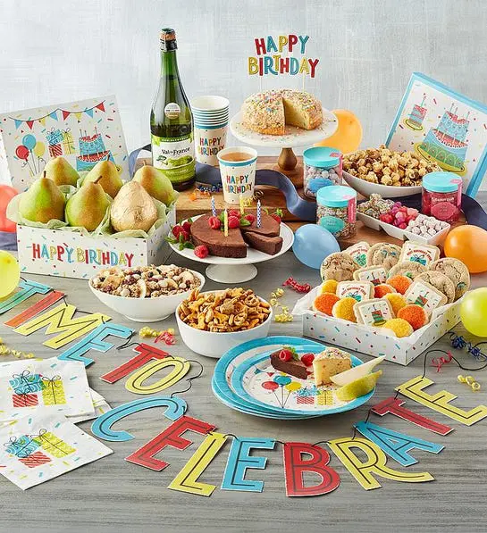 A photo of birthday gift ideas with a collection of fruit, chocolates, sweet and savory snacks on a table.