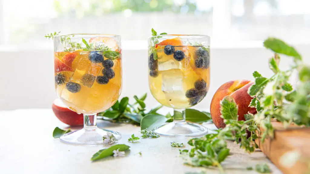 Two glasses of peach sangria with berries and mint.