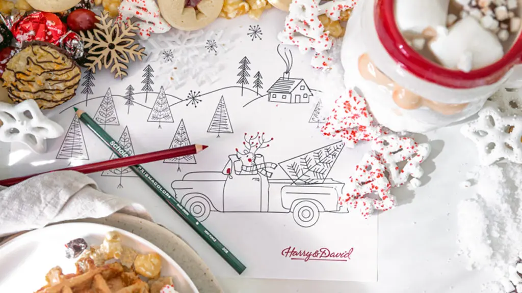 A photo of Christmas coloring pages surrounded by a mug of hot coco and cookies