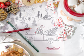 A photo of Christmas coloring pages surrounded by a mug of hot coco and cookies
