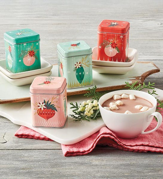 A photo of stocking stuffer ideas with a cup of hot cocoa next to four holiday tins on a cutting board.
