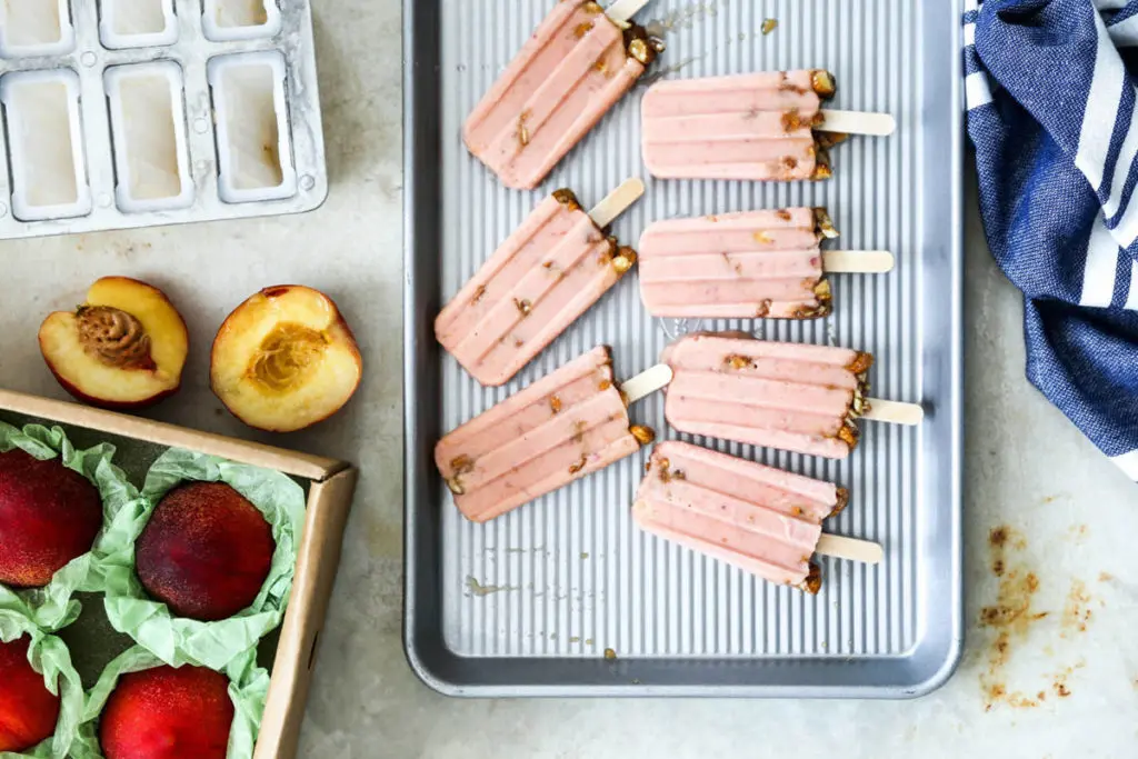 Homemade fruit popsicles on a cooking sheet next to a box of nectarines.