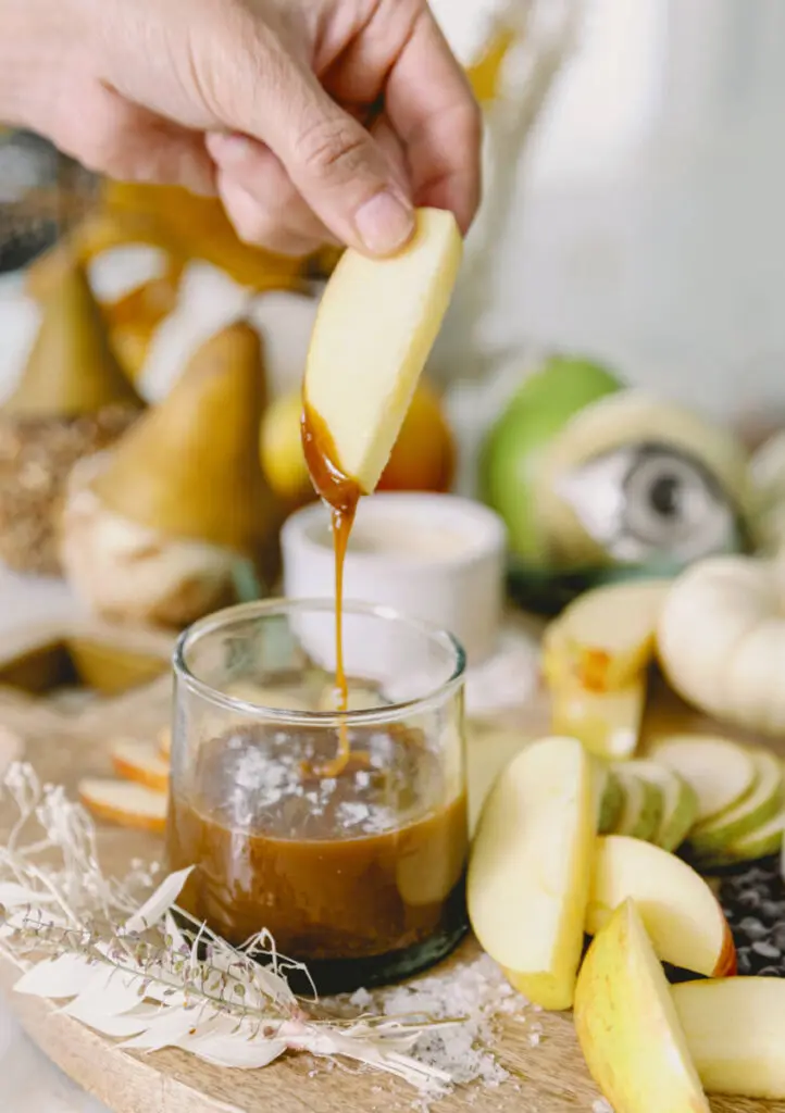 halloween snack board image - hand dipping a slice of pear into caramel dipping sauce