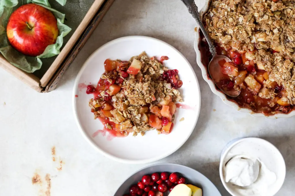 Apple cranberry crisp on a plate next to a large serving dish.