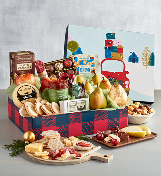 A photo of a gift guide with a box full of cookies, cheese, fruit, and chocolate with an array of the same ingredients on cutting boards in front of the box.