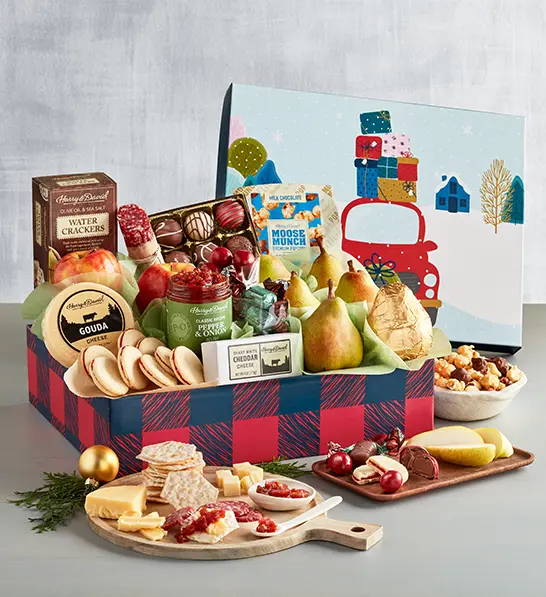 A photo of a gift guide with a box full of cookies, cheese, fruit, and chocolate with an array of the same ingredients on cutting boards in front of the box.