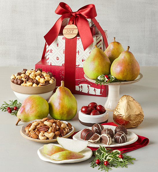 A photo of a gift guide with a stack of Christmas presents behind an array of pears, chocolates and nuts in bowls.