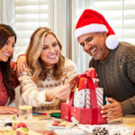 A photo of gifts under $50 with three people opening a gift box tower at a table