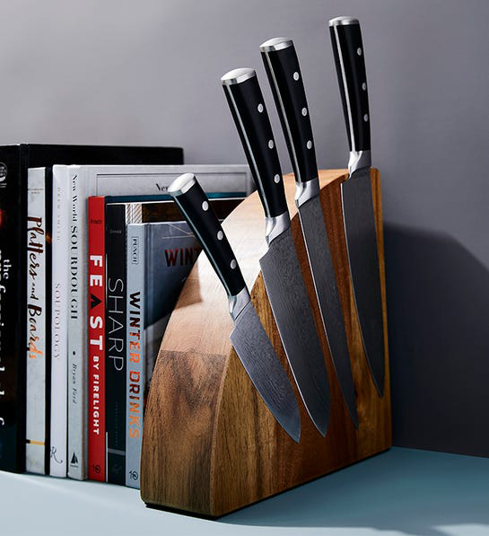 A photo of gift baskets with a magnetic acacia knife block next to a stack of cookbooks